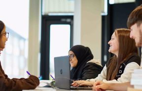 group of students working around table with laptop smiling