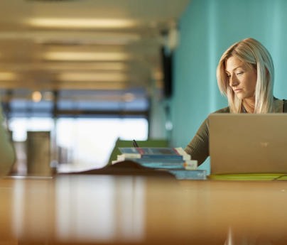 student sits with laptop and books in bright airy space