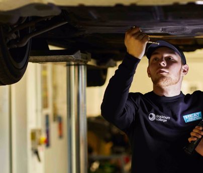 two students underneath a car doing mechanics in the HEAT Building.