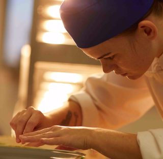 close up of student chef plating up food in industry kitchen