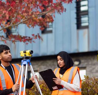 Students wearing hi-vis vests using surveying equipment on campus