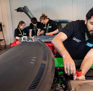 adult student working on engine of electric car