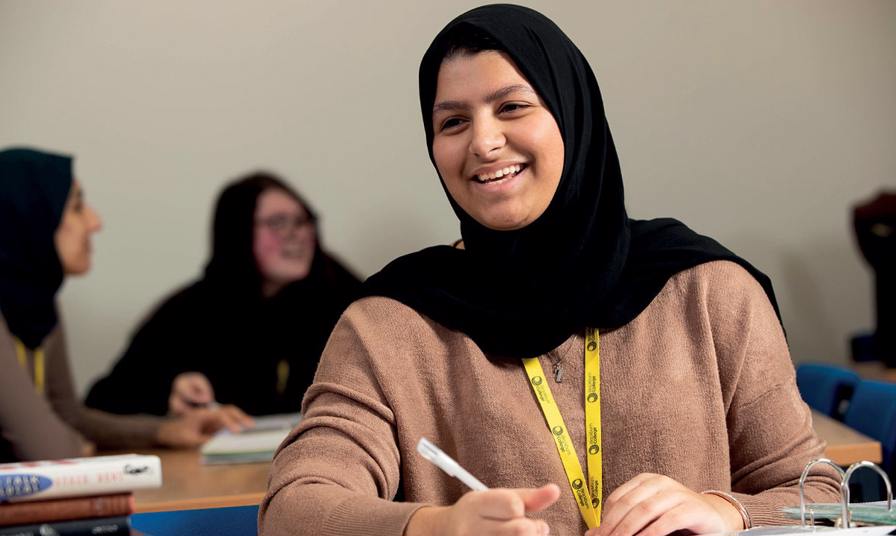 student wearing headscarf in classroom smiling doing work