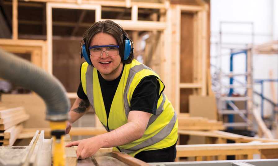 man wearing protective goggles and headphones operates joinery equipment